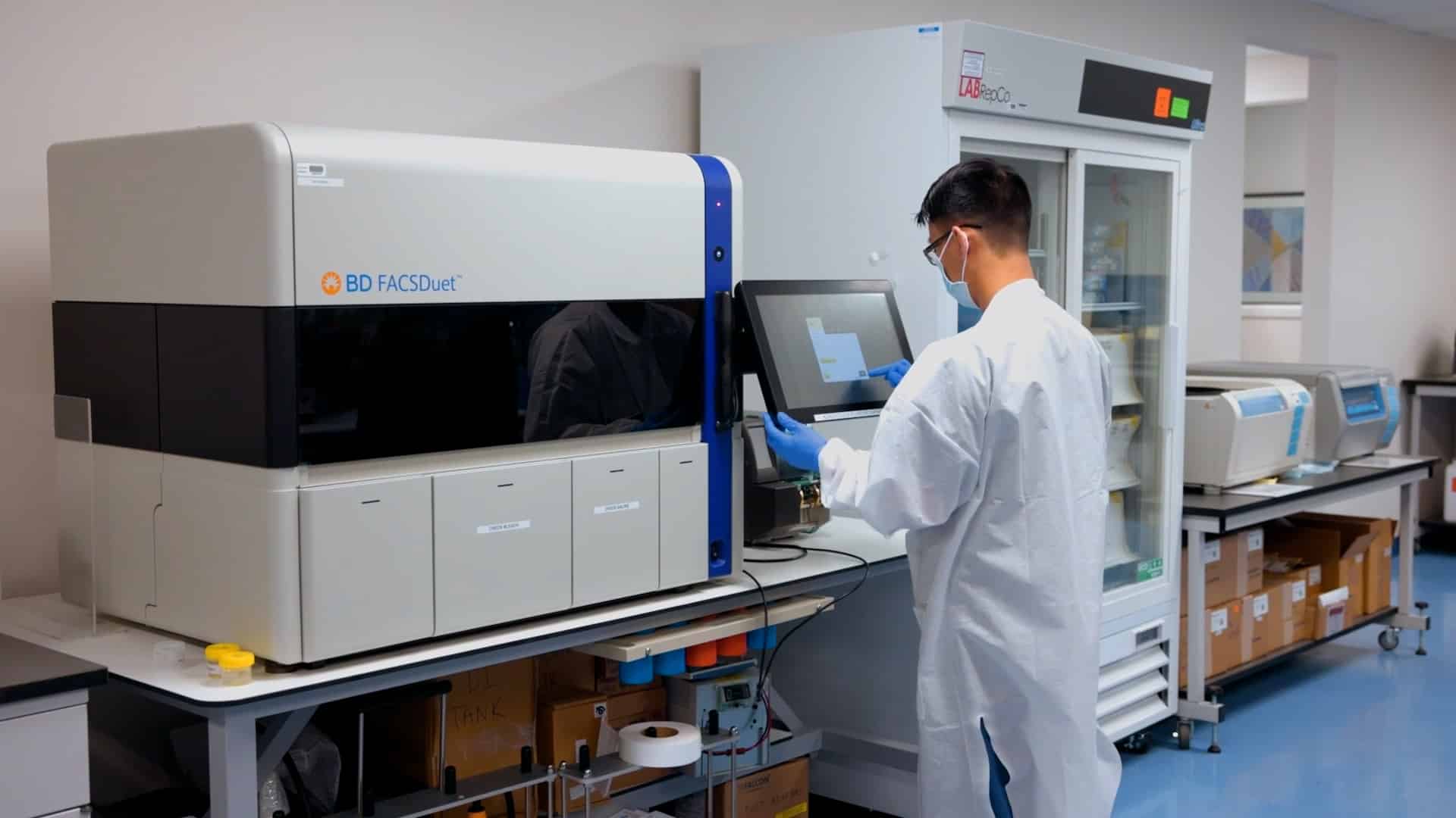 a scientist in a lab operating a BD FACASDuet sample preparation system